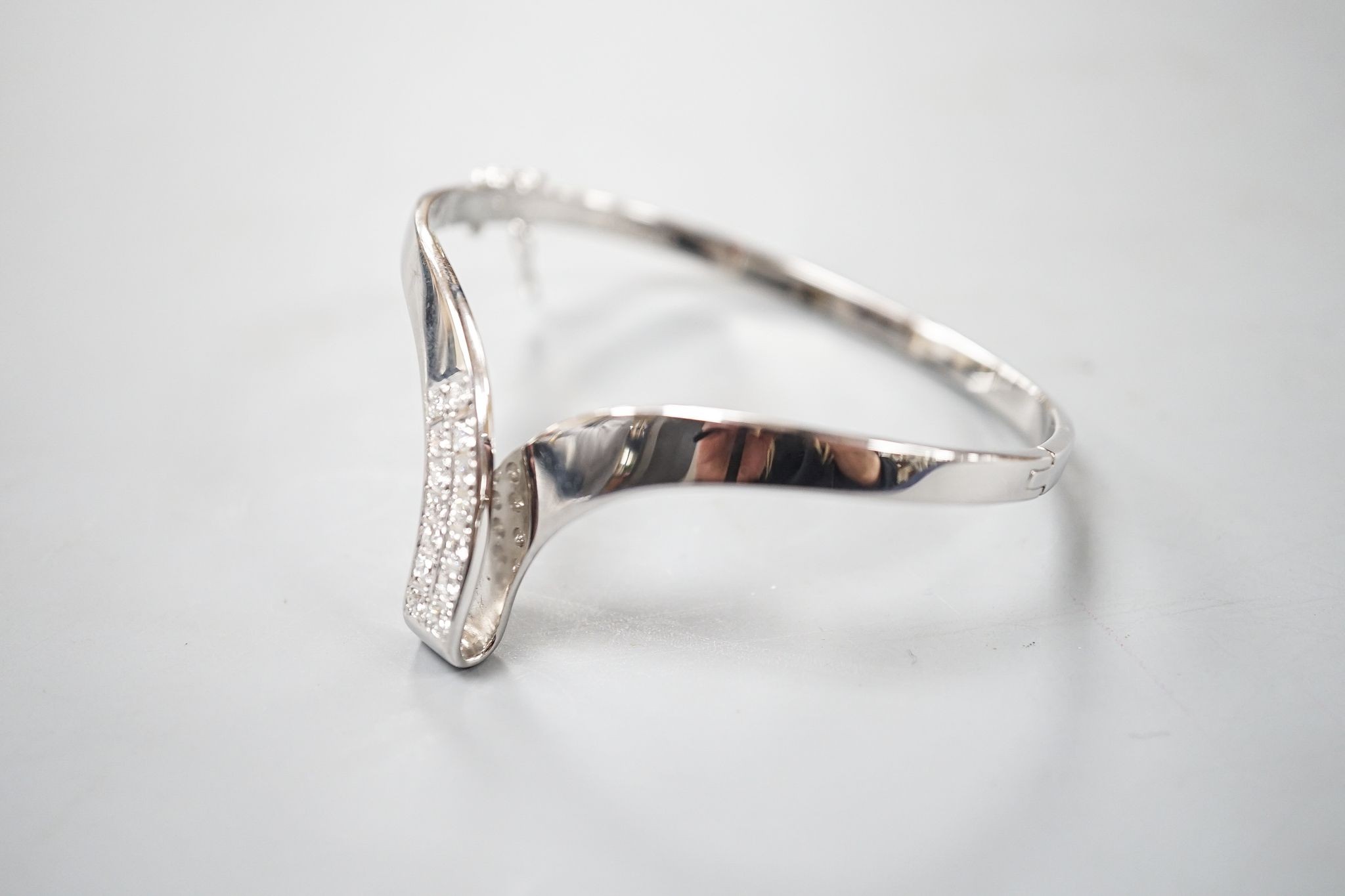 A modern 585 white metal and twelve stone diamond set wishbone shaped hinged bangle, gross 19.7 grams.